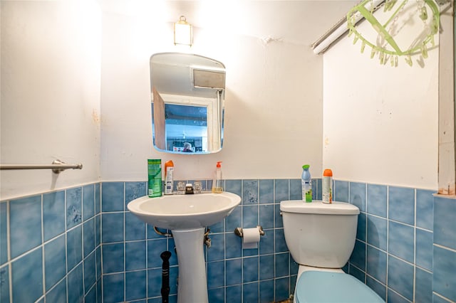 half bathroom featuring toilet, a wainscoted wall, and tile walls
