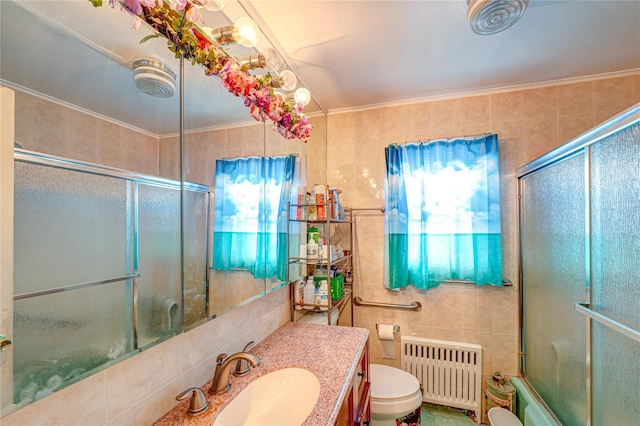 bathroom with radiator heating unit, toilet, vanity, tile walls, and bath / shower combo with glass door