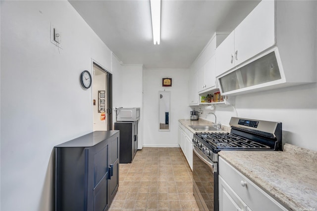 kitchen featuring stainless steel gas stove, open shelves, white cabinets, light countertops, and a sink
