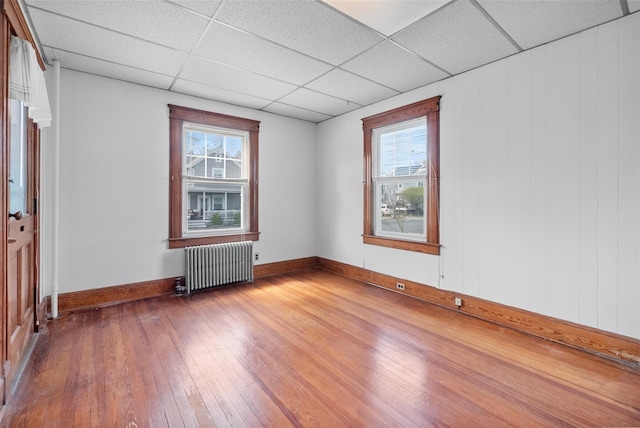 empty room with a paneled ceiling, radiator, plenty of natural light, and hardwood / wood-style flooring