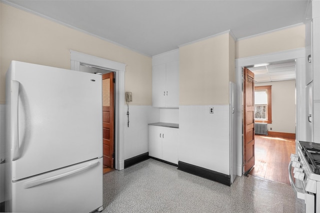 kitchen with freestanding refrigerator, radiator heating unit, white cabinetry, stainless steel gas range, and baseboards