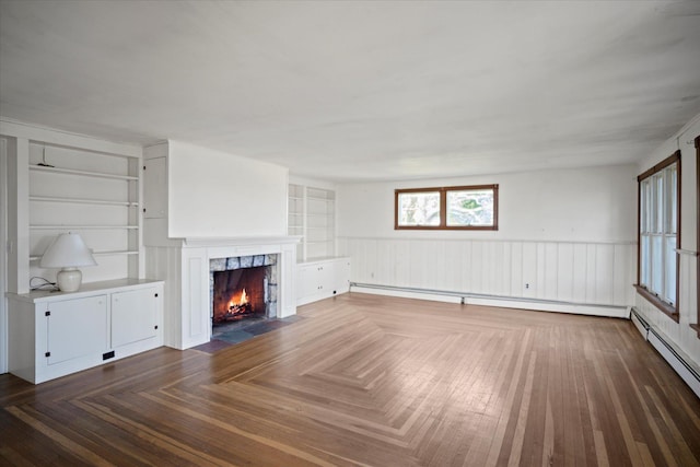 unfurnished living room with a fireplace, a baseboard heating unit, wainscoting, and built in features