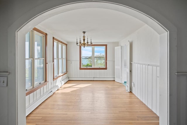 unfurnished dining area with light wood-style floors, a wainscoted wall, a chandelier, arched walkways, and a baseboard radiator