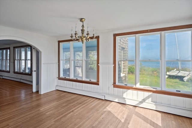 unfurnished dining area with baseboard heating, a chandelier, wood finished floors, a wainscoted wall, and arched walkways