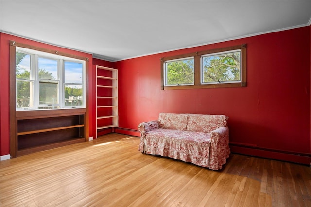 living area with baseboard heating, hardwood / wood-style floors, crown molding, and baseboards