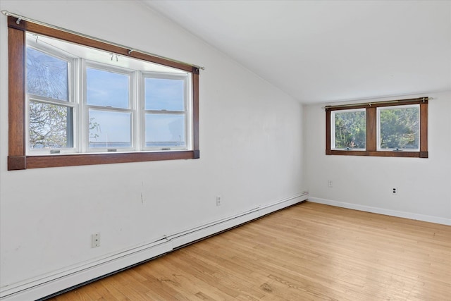 spare room featuring a baseboard heating unit, light wood finished floors, vaulted ceiling, and baseboards