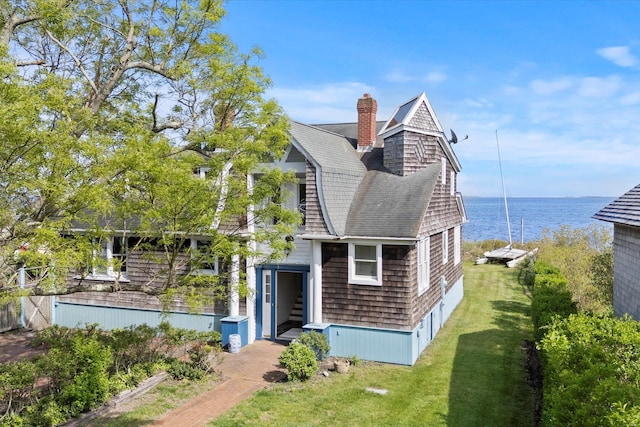 shingle-style home with a water view, roof with shingles, a front yard, and a chimney