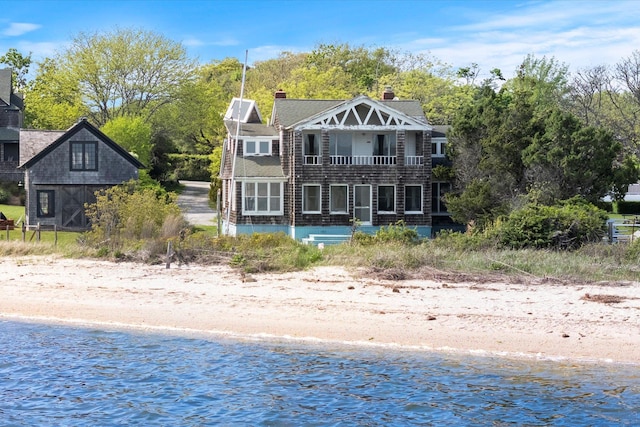 rear view of house with a balcony, view of water and beach, and a chimney