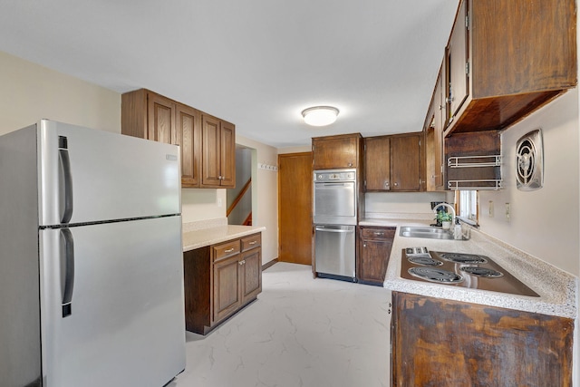 kitchen featuring light countertops, appliances with stainless steel finishes, brown cabinetry, and a sink