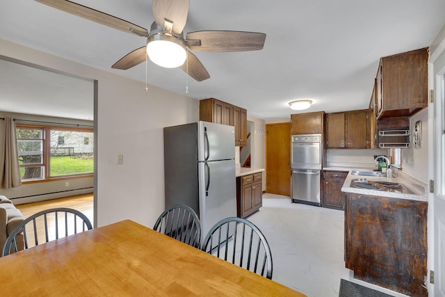 kitchen with freestanding refrigerator, a ceiling fan, light countertops, a baseboard heating unit, and a sink