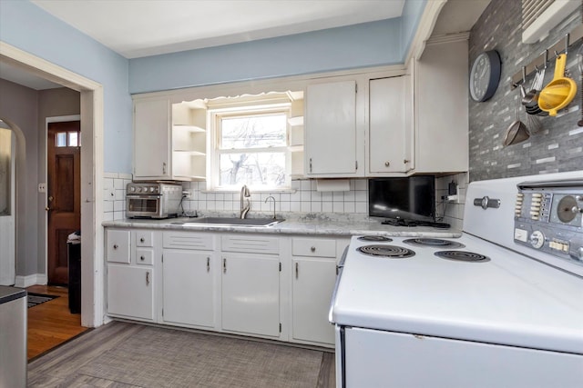 kitchen featuring backsplash, arched walkways, a sink, light countertops, and white range with electric stovetop