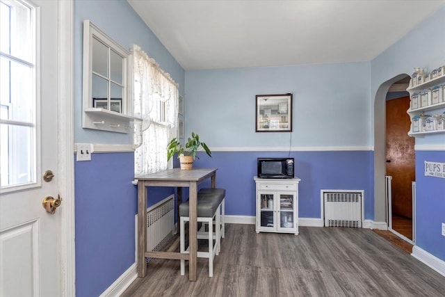 home office featuring radiator heating unit, arched walkways, baseboards, and wood finished floors