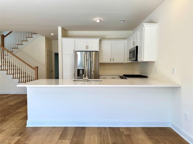 kitchen featuring a peninsula, white cabinetry, appliances with stainless steel finishes, wood finished floors, and light countertops