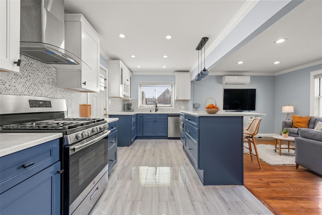 kitchen featuring wall chimney exhaust hood, ornamental molding, open floor plan, appliances with stainless steel finishes, and blue cabinets