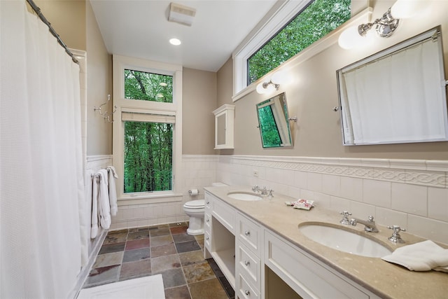 17 Eastwoods Rd, Pound Ridge, NY 10576 - full bathroom featuring wainscoting, double vanity, tile walls, toilet, and plenty of natural light