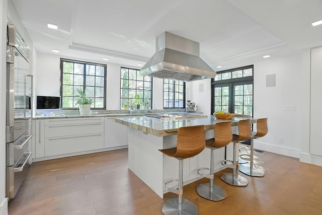 165 Valley Rd, New Rochelle, NY 10804 - kitchen featuring white cabinets, a kitchen island, island exhaust hood, and a healthy amount of sunlight