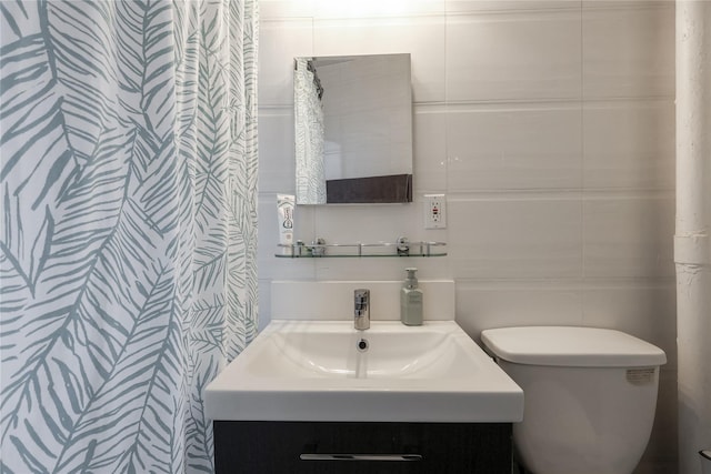 bathroom with toilet, vanity, and tile walls
