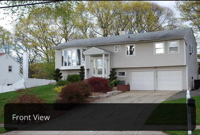 raised ranch featuring concrete driveway, a chimney, an attached garage, central AC unit, and fence