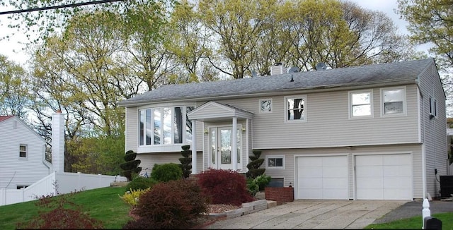 bi-level home featuring a chimney, an attached garage, fence, and concrete driveway