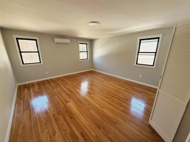 unfurnished room with baseboards, wood finished floors, and a wall mounted AC