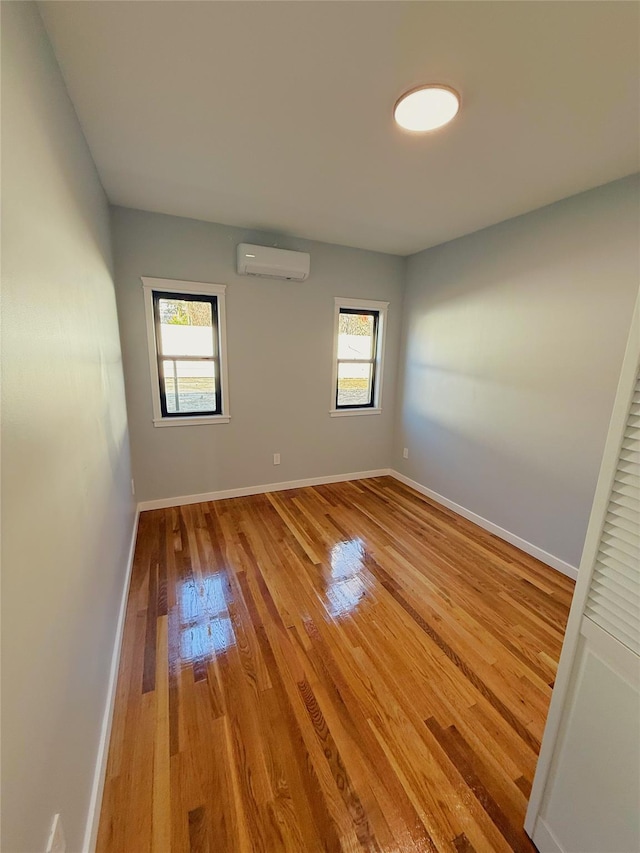 empty room with an AC wall unit, baseboards, light wood-type flooring, and a healthy amount of sunlight