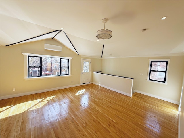 unfurnished living room with crown molding, light wood-style floors, baseboards, lofted ceiling, and a wall unit AC