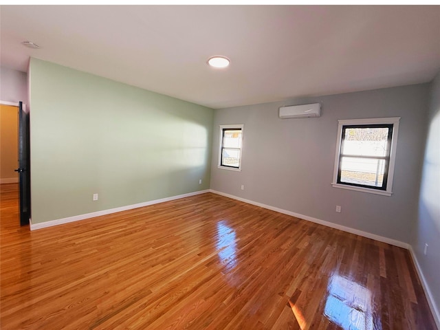 spare room with light wood-style floors, a wall unit AC, and baseboards