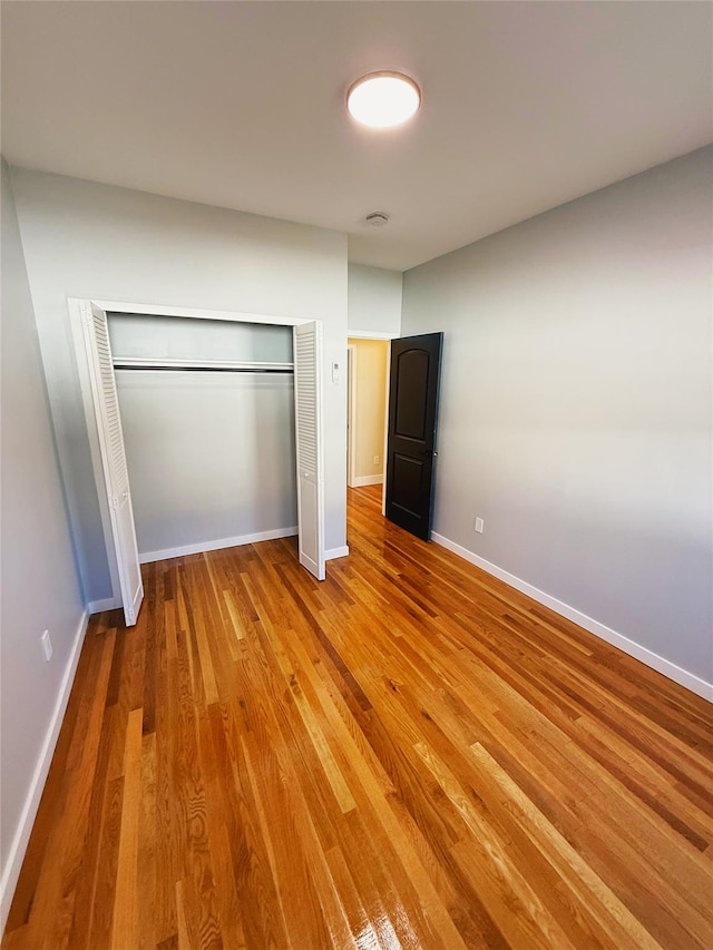 unfurnished bedroom featuring baseboards, wood finished floors, and a closet