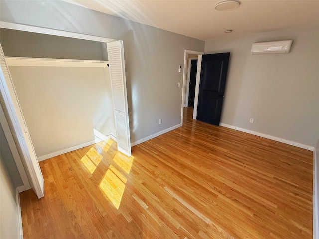 unfurnished bedroom with light wood-type flooring, baseboards, an AC wall unit, and a closet