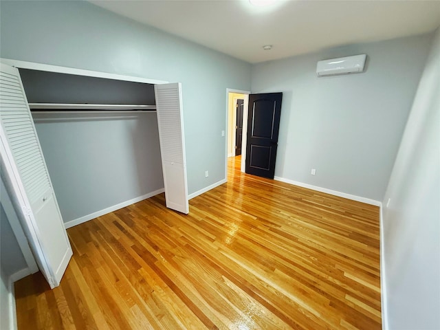 unfurnished bedroom with baseboards, light wood-style flooring, an AC wall unit, and a closet