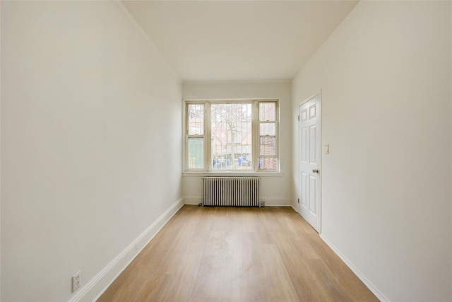 spare room with light wood finished floors, baseboards, and radiator