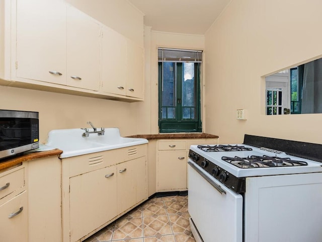 kitchen with stainless steel microwave, white range with gas cooktop, crown molding, and light tile patterned flooring