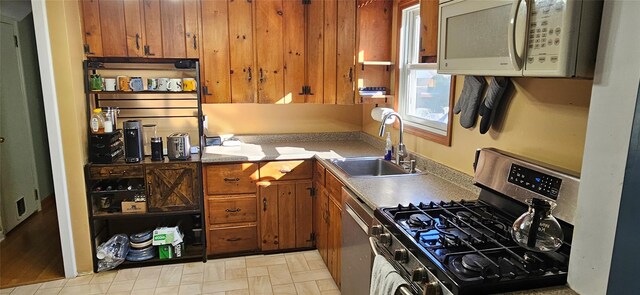 kitchen with appliances with stainless steel finishes, wood walls, light countertops, a sink, and brown cabinets