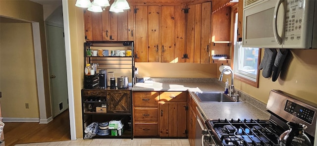 kitchen with a chandelier, white microwave, stainless steel range with gas cooktop, brown cabinetry, and a sink