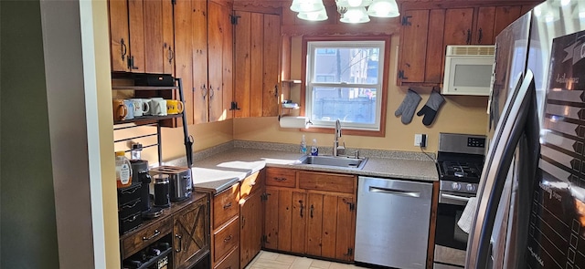kitchen featuring brown cabinetry, appliances with stainless steel finishes, a sink, light countertops, and a notable chandelier