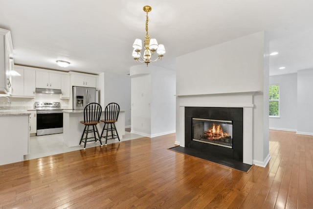 living room featuring light wood finished floors, a fireplace with flush hearth, recessed lighting, a chandelier, and baseboards