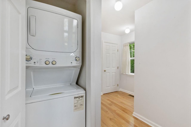 laundry room featuring stacked washer and clothes dryer, light wood finished floors, and baseboards