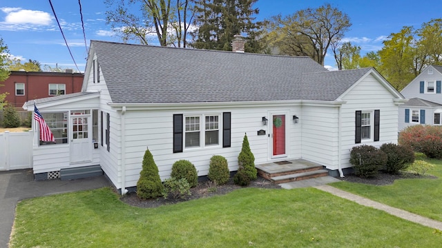 view of front of property featuring a sunroom, a front lawn, roof with shingles, and a chimney