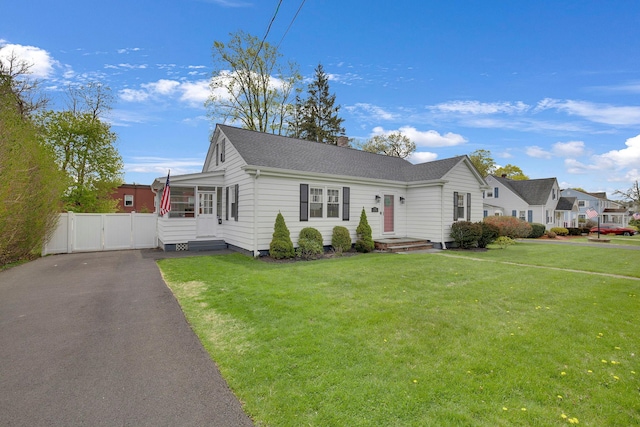 view of front of property featuring a shingled roof, aphalt driveway, a sunroom, a front yard, and a gate