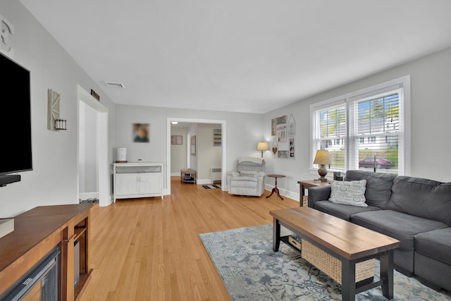 living area featuring baseboards, visible vents, radiator heating unit, and light wood finished floors