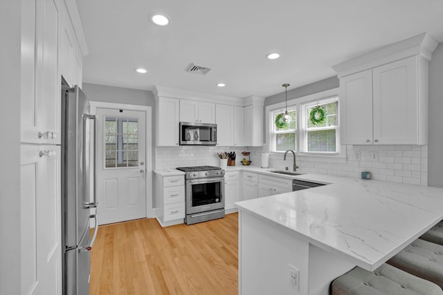 kitchen featuring a peninsula, plenty of natural light, white cabinets, a sink, and stainless steel appliances