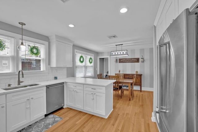 kitchen with visible vents, a peninsula, white cabinetry, a sink, and appliances with stainless steel finishes