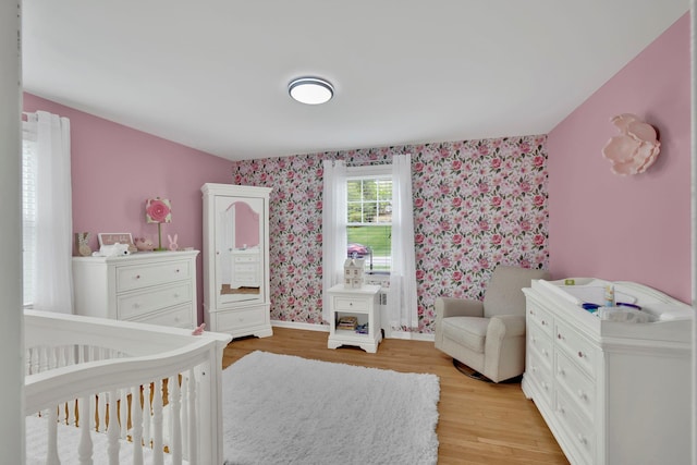 bedroom with light wood-style floors, a crib, baseboards, and wallpapered walls