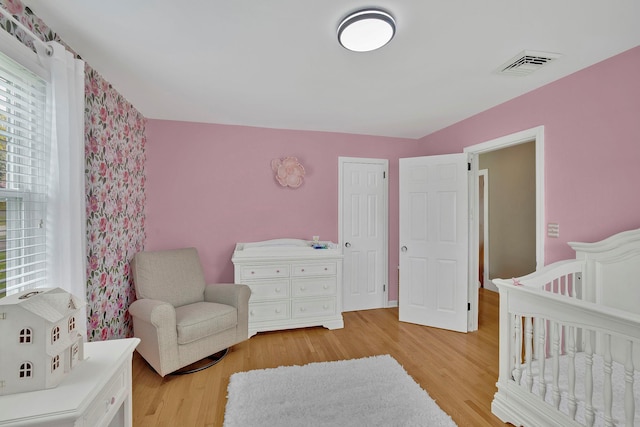bedroom featuring a nursery area, multiple windows, light wood-type flooring, and visible vents
