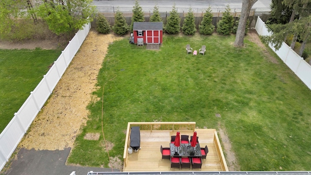 view of yard with a storage unit, outdoor dining space, a wooden deck, a fenced backyard, and an outdoor structure