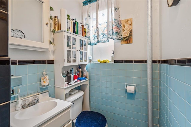 bathroom with toilet, tile walls, wainscoting, and vanity