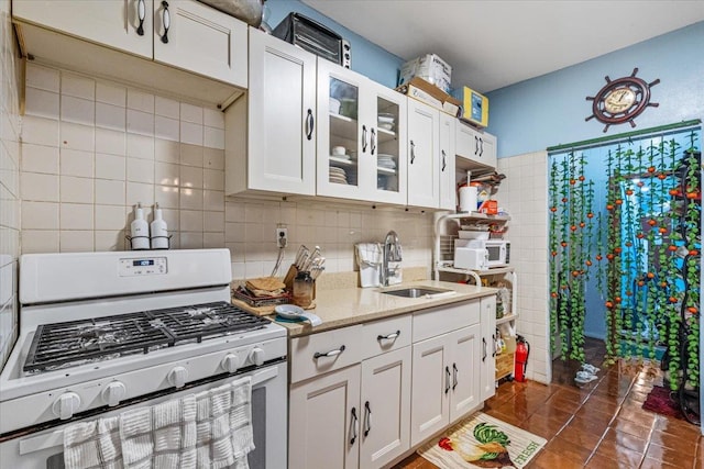 kitchen featuring white gas stove, white cabinets, glass insert cabinets, and a sink