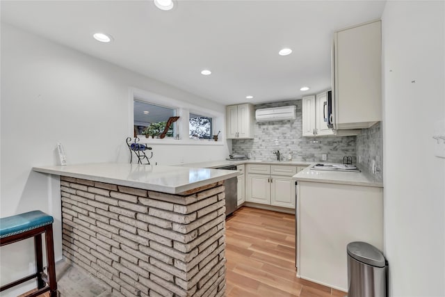 kitchen featuring dishwasher, a wall mounted air conditioner, a peninsula, light wood-type flooring, and light countertops