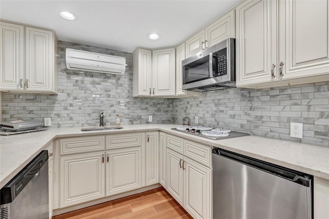 kitchen with appliances with stainless steel finishes, a wall unit AC, a sink, tasteful backsplash, and light stone countertops