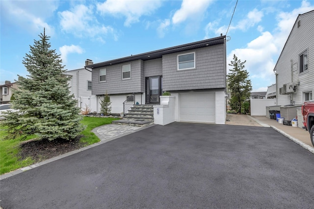 raised ranch with an attached garage, asphalt driveway, and a chimney